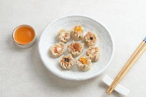 mini dim sum kinesiska dumplings serveras på vit tallrik, med sås och ätpinne. närbild. foto
