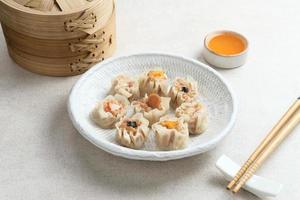 mini dim sum kinesiska dumplings serveras på vit tallrik, med sås och ätpinne. närbild. foto
