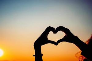 siluett händer som bildar hjärtform med solnedgången foto