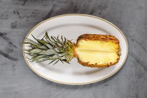 vit tallrik med mogen skivad ananas på grå betongbakgrund. foto