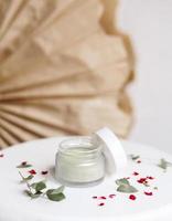 pulver kosmetisk mask. glasburk med matcha på en vit bakgrund med torra kronblad. foto