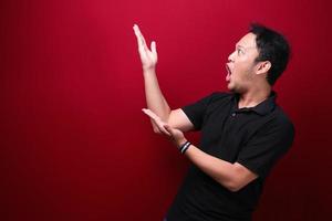 ung asiatisk man är förvånad och skriker wow med att peka höger med handen isolerad på röd bakgrund. foto