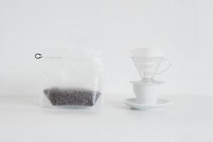 kaffebönor i förpackning och dropp kaffebryggare på vit kopp med bricka isolerad på vit bakgrund foto