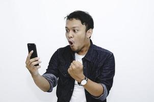 ung asiatisk man chockad när han tittar och pekar smartphone foto