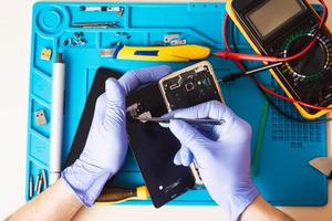 hantverkare i gummihandskar reparera eller serva en mobiltelefon på en speciell gummimatta för reparation. utsikt från insidan foto