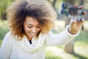 ung afrikansk amerikansk flicka selfie i parken med en smartphone foto