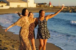 tre roliga multietniska flickor som bär sommarklänning skrattar och har roligt tillsammans på stranden. foto