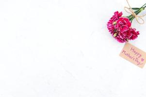 maj mors dag idékonceptfotografering - vackra blommande nejlikor bundna av rosett med krafttextkort isolerat på ljust modernt bord, kopieringsutrymme, platt liggande, ovanifrån, mock up foto