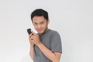 asiatisk man allvarligt ansikte och skarp ser med att dölja telefonen gest isolerade grå bakgrund. foto
