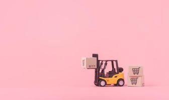 logistik och leveransservice - gaffeltruckmodell och papperskartonger eller paket med en kundvagnslogotyp på rosa bakgrund. shoppingtjänst på webben och erbjuder hemleverans. foto