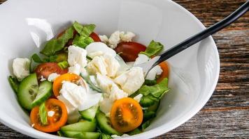 grönsaker sallad med dressing inuti vit skål på rustika bord foto