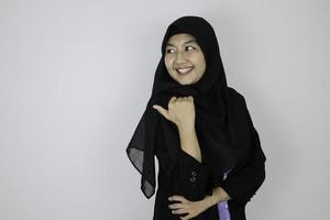 leende ung asiatisk islam kvinna som bär huvudduk är leende och pekar bakom. foto