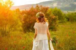 kvinna som går på ett fält av blommor vid solnedgången med en krans på huvudet foto