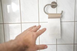 man hand försöker ta sista biten av toalettpapper rulle i badrummet, närbild, detaljer. foto