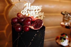 stor svart födelsedagstårta med färsk frukt och godis på ett festligt bord. godisbit. bord med olika godis för fest foto