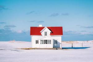 litet vitt hus med rött tak och blå himmel på snöig foto