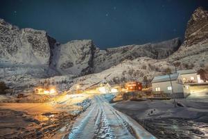 norska färgglada by omgiven snö berg med stjärnklara på natten foto