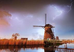 blixt på molnig mörk himmel. traditionella holländska väderkvarnar kanal foto