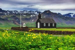 bergsutsikt, island. vacker svart träkyrka i budir. foto