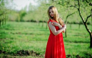 porträtt av ljust hår flicka på röd klänning bakgrund vårträdgård. foto