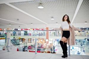 ung lockig modell tjej poserade på minikjol på stort köpcentrum nära glasräcken. foto