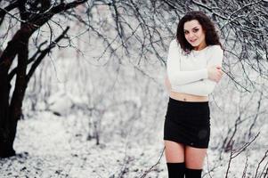 lockig brunett flicka bakgrund fallande snö, slitage på svart mini kjol och ull strumpor. modell på vintern. modeporträtt vid snöväder. instagram-tonat foto. foto
