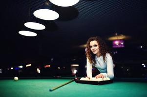 ung lockig flicka poserade nära biljardbord. sexig modell på svart minikjol spela rysk snooker. spela spel och roligt koncept. foto