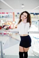 ung lockig modell tjej talar i telefon på stort köpcentrum nära glasräcken. foto