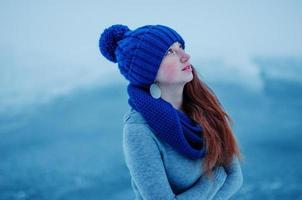 porträtt av ung rött hår flicka med fräknar bär på blå stickad ull mössa och halsduk i vinter dag bakgrund is. foto