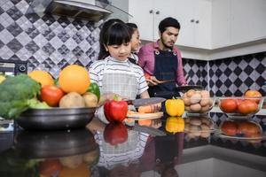 asiatiska familjer lagar mat och föräldrar lär sina döttrar att laga mat i köket hemma. familjeaktiviteter på semester och glad i rekreation koncept foto