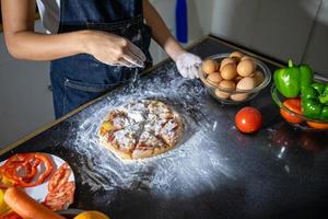 asiatiska kvinnor förbereder en pizza, knådar degen och lägger ingredienserna på köksbordet foto