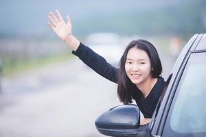 vacker asiatisk kvinna leende och njuter. kör bil på väg för resor foto