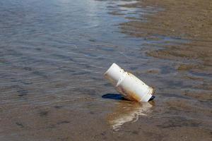 plastmugg kvar på stranden efter att turisterna tagit semester. sopor på sandstranden. plastglas i havet. foto