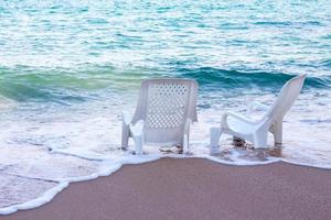 tomma vita plaststolar på stranden med vackra vita havsvågor. foto