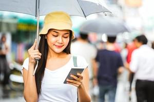 asiatisk kvinna med paraply och smartphone bland regn. foto