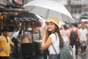 unga vuxna asiatiska resenärer håller paraply när det regnar på gågatan. foto