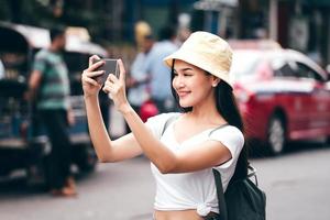 ung asiatisk kvinna med smart telefon. khaosan väg bakgrund. foto