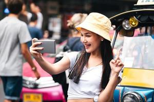 asiatisk resenär glad kvinna selfie med tuktuk thailändsk stil taxi. foto
