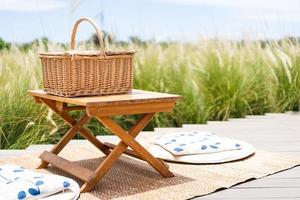 flätad picknickkorg på träbord på utomhus med naturens blommande blomsterfält foto