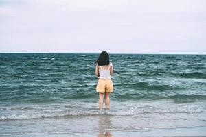 porträtt av ung vuxen asiatisk kvinna bakifrån koppla av på stranden på dagar. foto