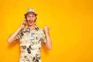 en glad manlig turistresenär pratar i telefon och gläds åt de goda nyheterna genom att peka finger mot en tom plats för reklam. isolerad på en gul bakgrund med plats för text foto