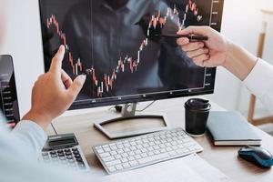investerare pekar på bärbara datorer som har investeringsinformation på aktiemarknaderna och partners som tar anteckningar och analyserar resultatdata. foto
