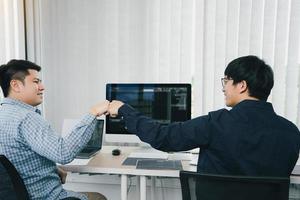 asiatiska anställda mjukvaruutvecklare firar framgångsprojekt med knytnäve i kontorsrummet. foto