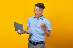 upphetsad ung asiatisk man asiatisk i glasögon med bärbar dator isolerad på gul bakgrund. affärsman och entreprenör koncept foto