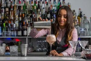 kvinnlig barkeeper häller cocktail i glas foto