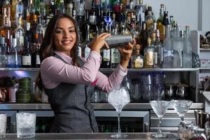 glad kvinnlig bartender med shaker förbereder cocktail foto