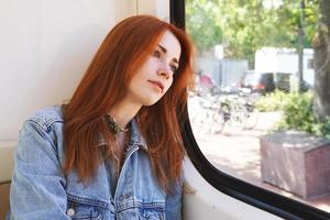 ung kvinna sitter i spårvagn eller spårvagn tittar ut genom fönstret foto