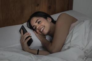 kvinna som använder smartphone i sängen på kvällen foto