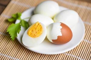 ägg matlagning hälsosam kost koncept, ägg frukost, färska skalade ägg meny mat kokt ägg och äggskal på vit platta dekorerad med blad grön selleri på trä bakgrund foto