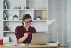 asiatiska frilanskvinnor använder laptop och rött kreditkort för att handla online på bordet. onlinebetalning online finansiella transaktioner. frilansarbete som säljer online. foto